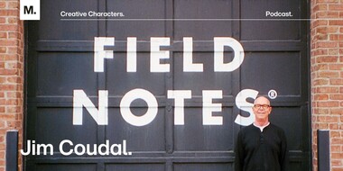 Field Notes founder Jim Coudal standing in front of a black and white mural that reads "Field Notes."